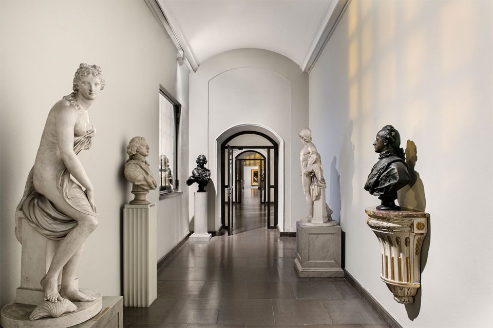 Korridorformat museisal med skulpturer och byster i vitt och svart längst med väggarna.