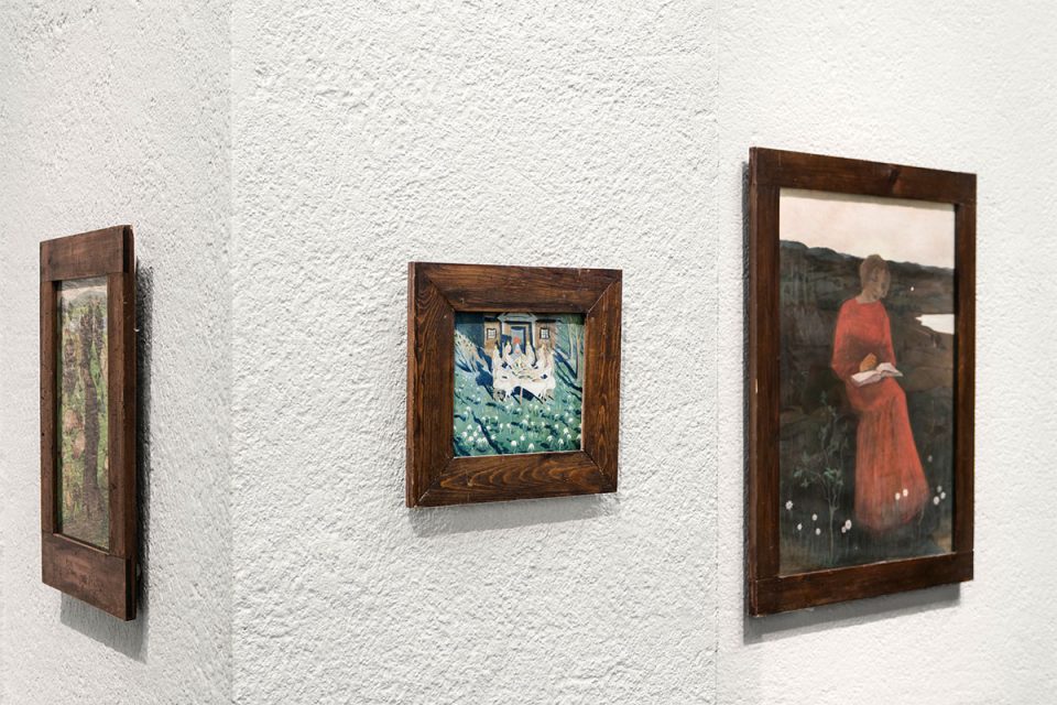Närbild på tre mindre målningar i träram mot vit vägg.
