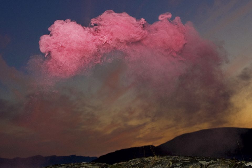 Vy av landskap med karga berg, himmel som skiftar från organge till blå med kraftigt rosa moln högst upp.