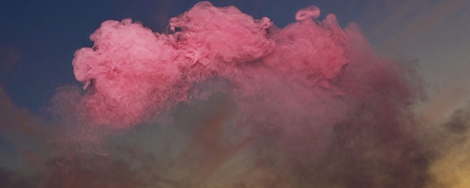 Vy av landskap med karga berg, himmel som skiftar från organe till blå med kraftigt rosa moln högst upp.