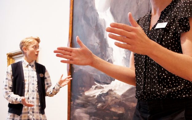 En konstpedagog och en teckenspråkstolk står framför en målning i en museisal.