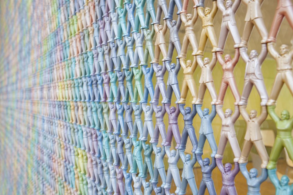 En väggskärm byggd av många små människofigurer i pastellfärger som hakar i varandra